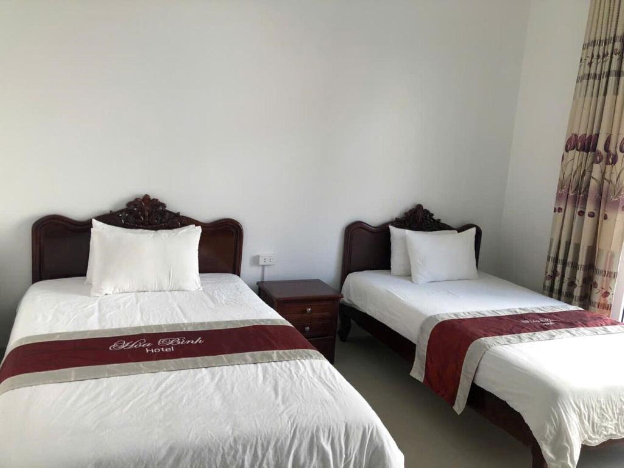 A hotel room with two beds, each with a wooden headboard, white bedding, and a red and white striped bed runner.