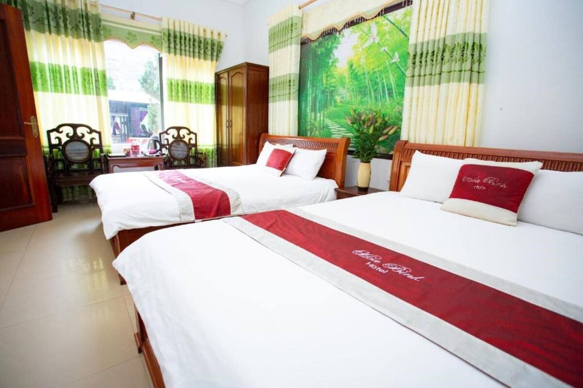A hotel room with two beds, a wooden wardrobe, a desk, and a large window with curtains.