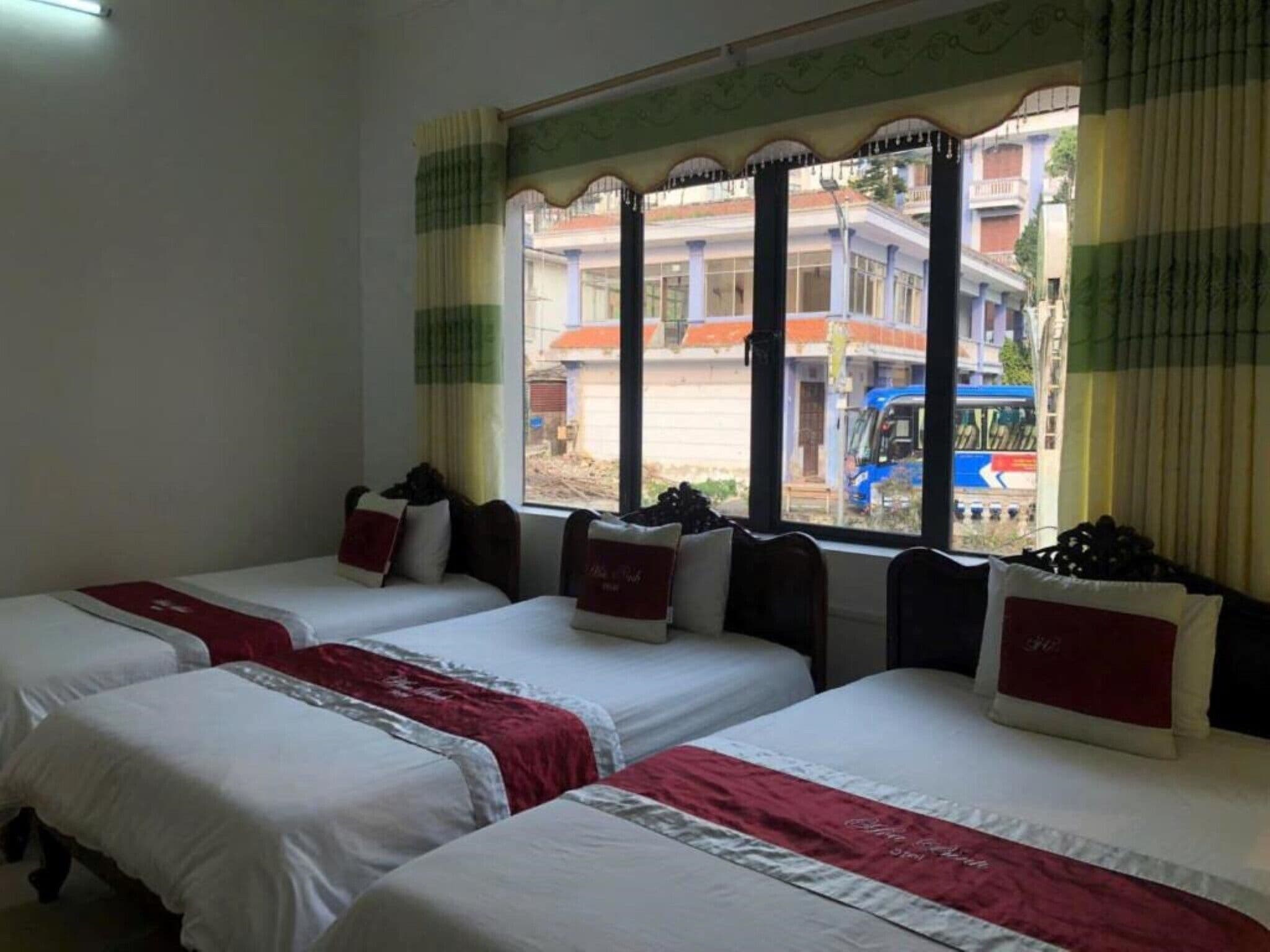 A hotel room with two single beds, each with a red and white bedspread, and a window with a view of buildings and a blue vehicle outside.