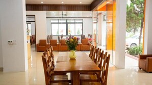 Un comedor amplio con una larga mesa de madera y sillas, un jarrón de flores y vistas al exterior a través de grandes ventanales.