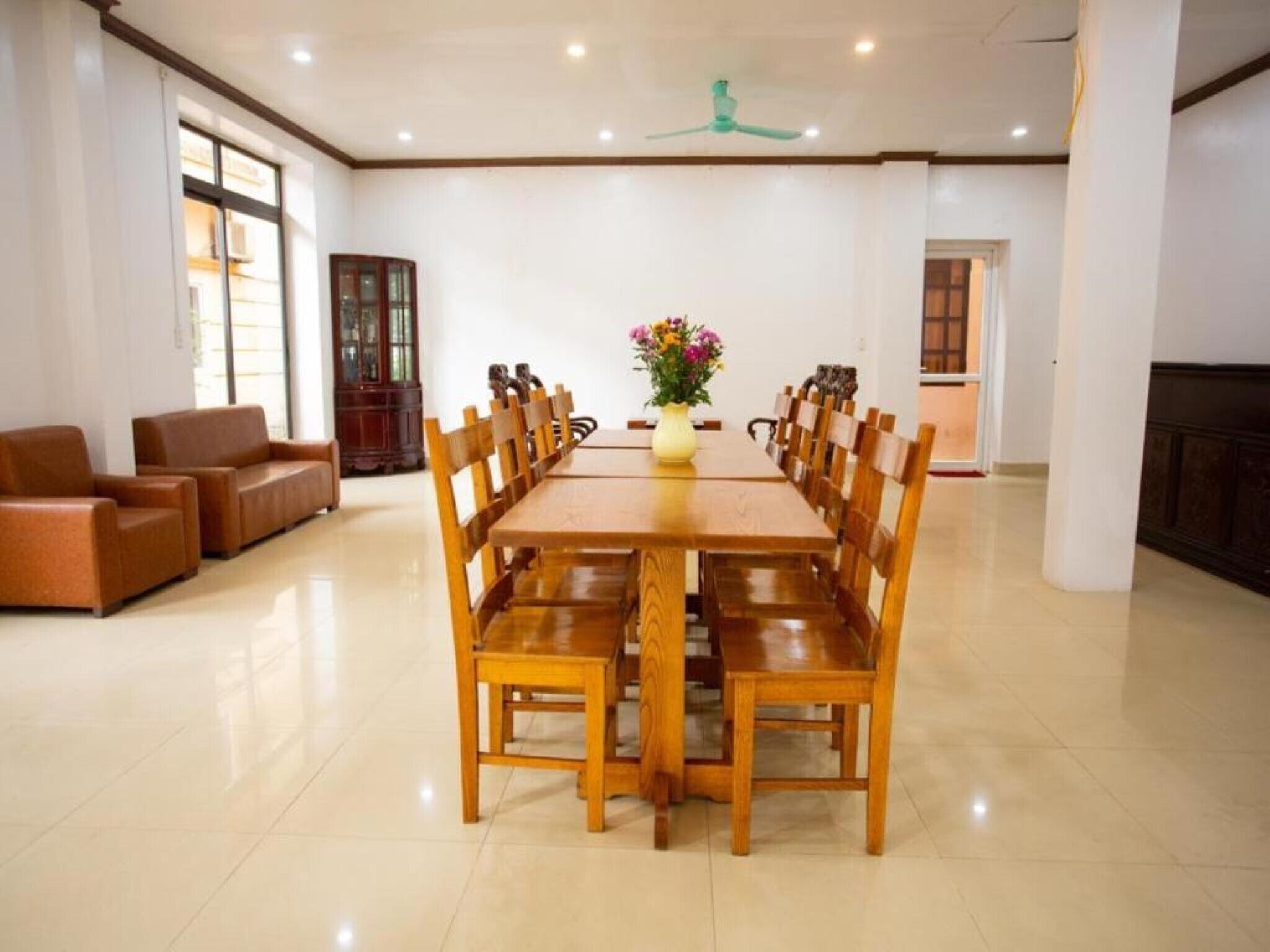 A dining area with a wooden table and chairs, a vase with flowers, and a cabinet in the background.