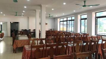 A spacious dining area with multiple tables and chairs, ceiling fans, and large windows providing natural light.