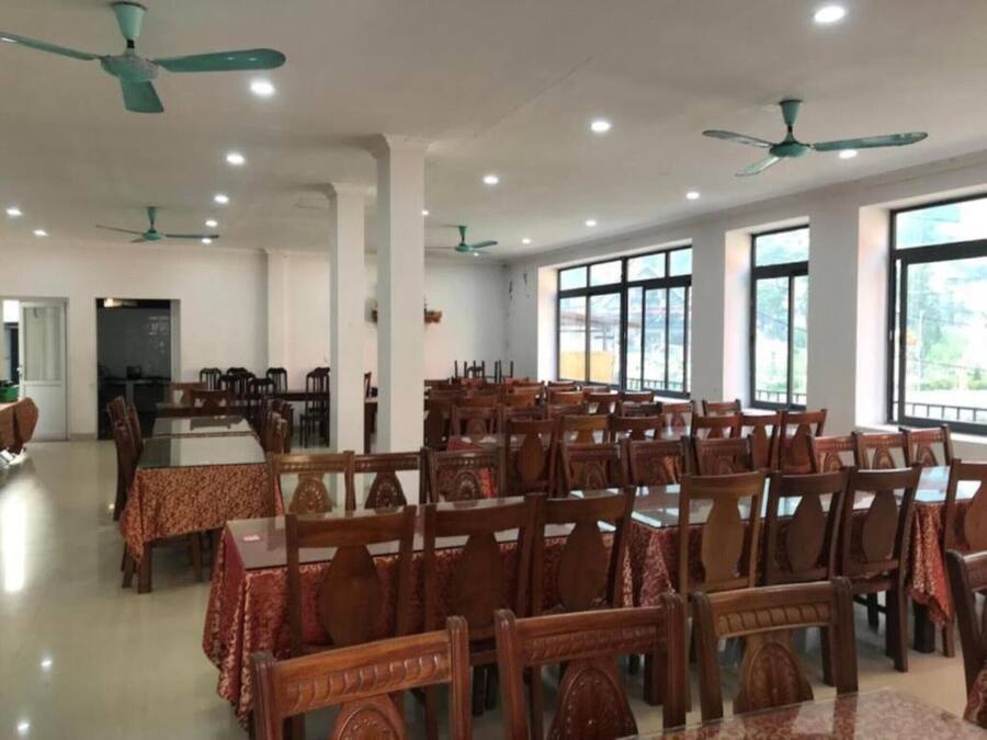A spacious dining area with multiple tables and chairs, ceiling fans, and large windows providing natural light.