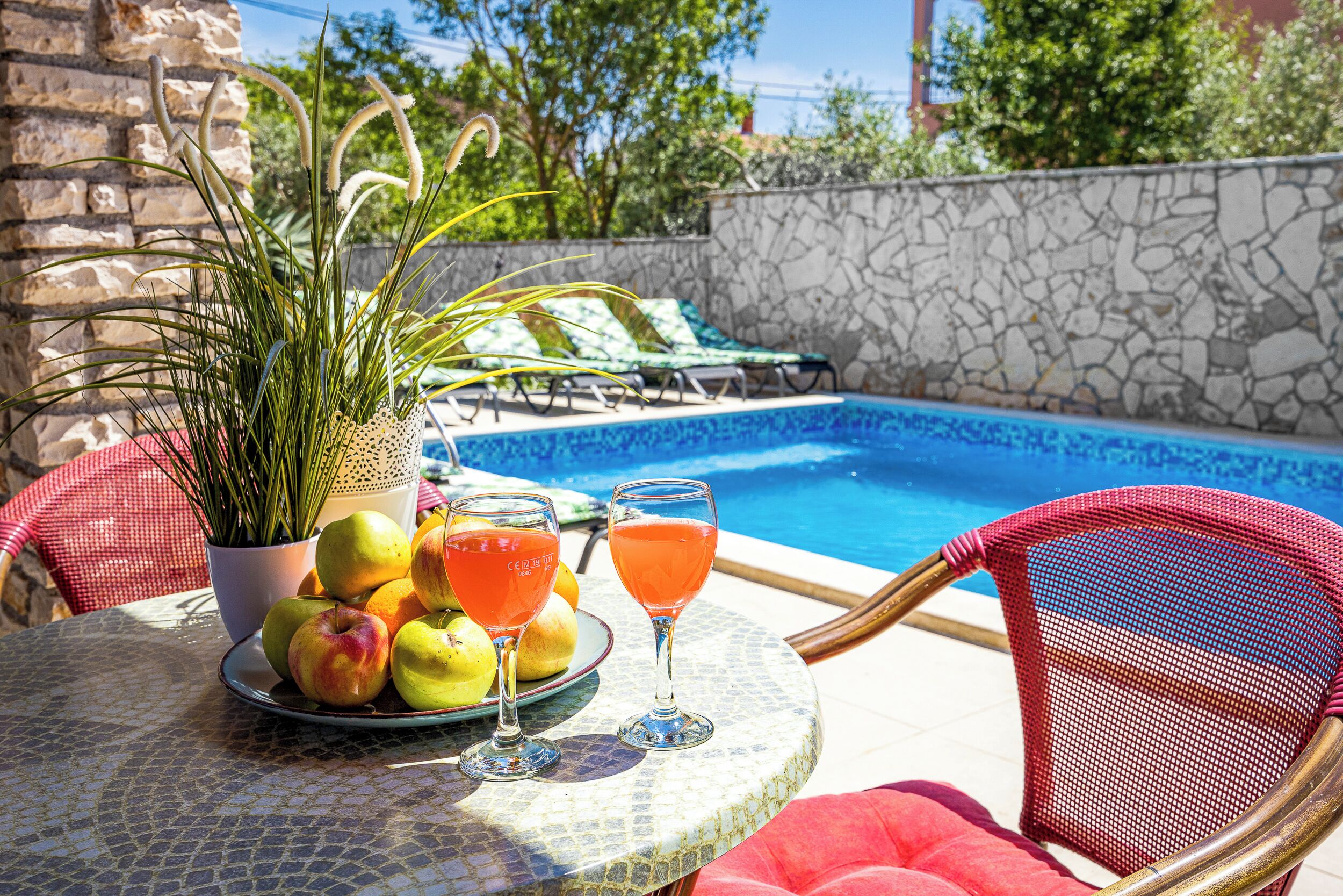 A poolside table with fruits, drinks, and a potted plant.