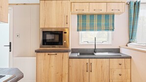 A compact kitchen with wooden cabinets, a built-in microwave, a sink, and a window with plaid curtains.