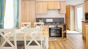 A modern kitchen with wooden cabinets, a gas stove, an oven, and a dining area with white chairs and a table.