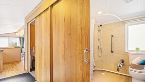 A modern bathroom with a wooden door, a shower, a toilet, and a window.