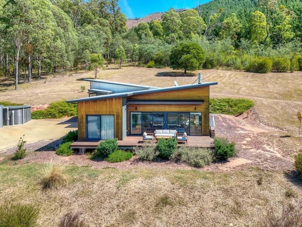 Ein modernes Haus mit einer Terrasse, umgeben von trockenem Gras und Bäumen.