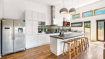 A modern kitchen with white cabinetry, a central island with stools, stainless steel appliances, and large windows.