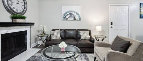 A living room with a fireplace, a round glass coffee table, a sofa, and a door.