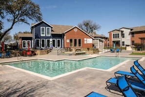 Ein Schwimmbecken mit Liegestühlen, eine überdachte Terrasse und ein Gebäude mit Backsteinfassade.