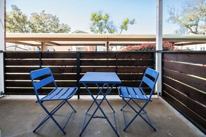A patio with two blue folding tables and chairs, a wooden fence, and a covered area in the background.