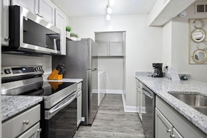 Una cocina moderna con electrodomésticos de acero inoxidable, encimeras de granito y suelo gris.