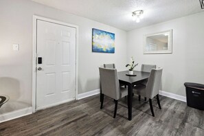 A dining area with a white door, a painting, a mirror, and a trash bin.