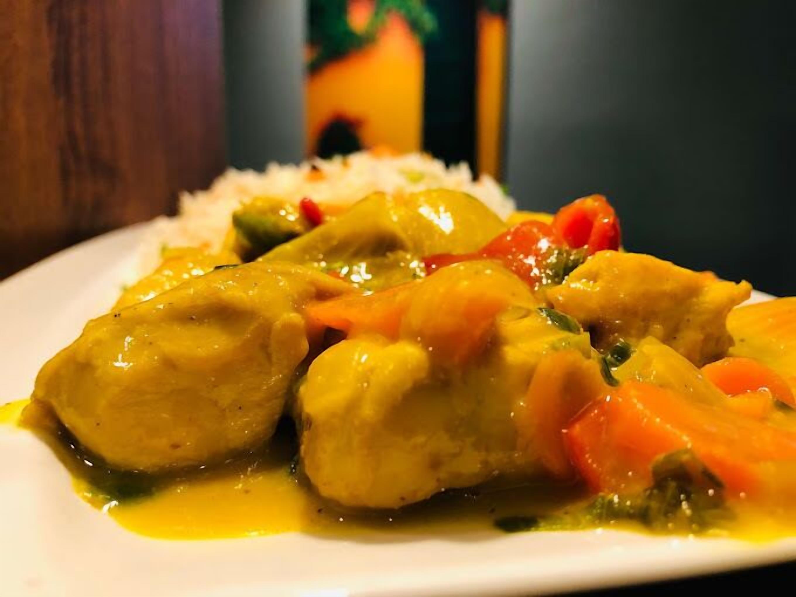 Une assiette de curry de poulet, accompagné de légumes et de riz.