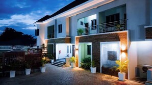 A modern two-story house with a balcony, a covered entrance, and potted plants. - D'Stolz Villa and Hospitality (Abuja)
