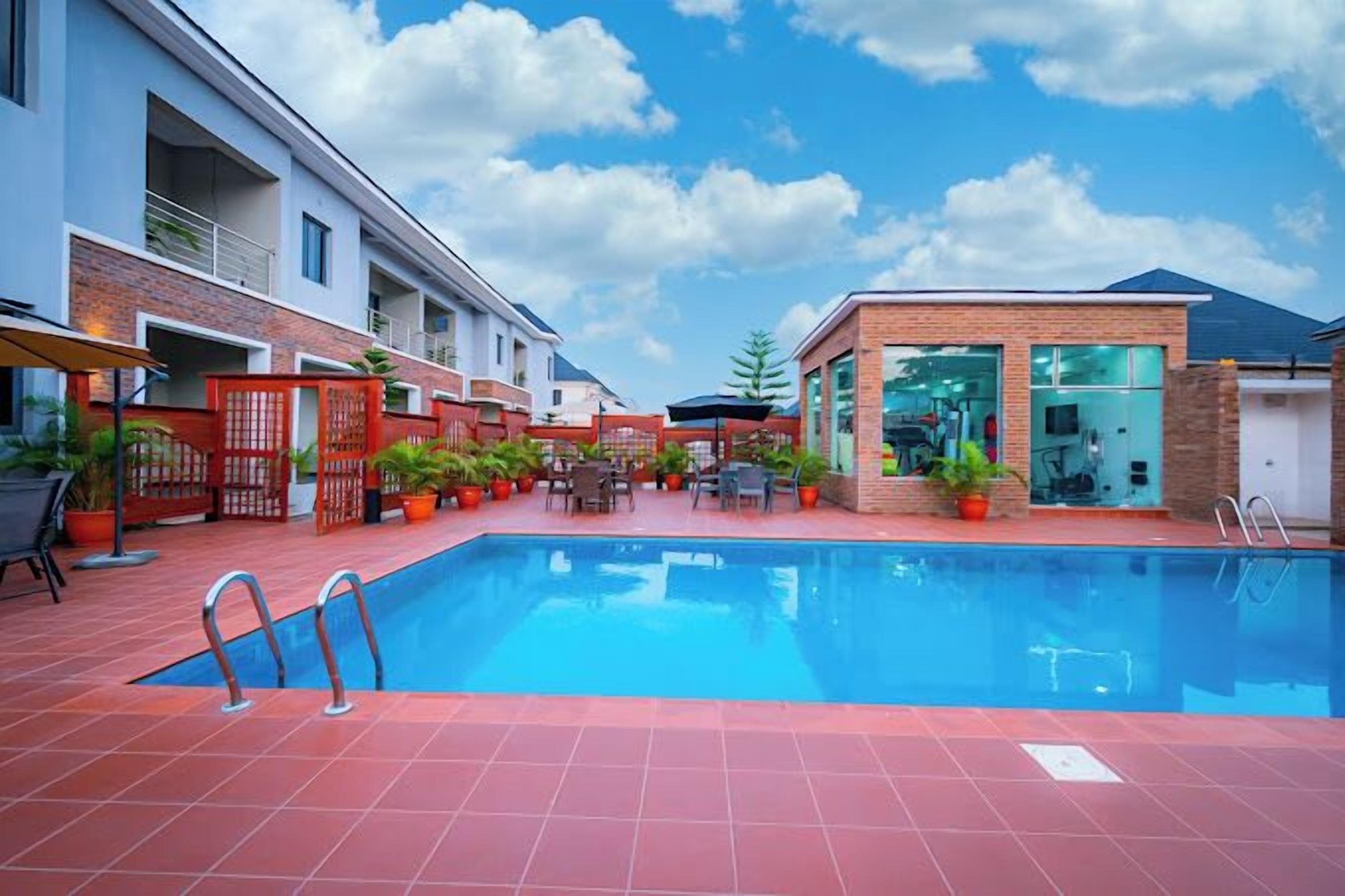 A swimming pool with a red-tiled deck, surrounded by potted plants and outdoor furniture.
