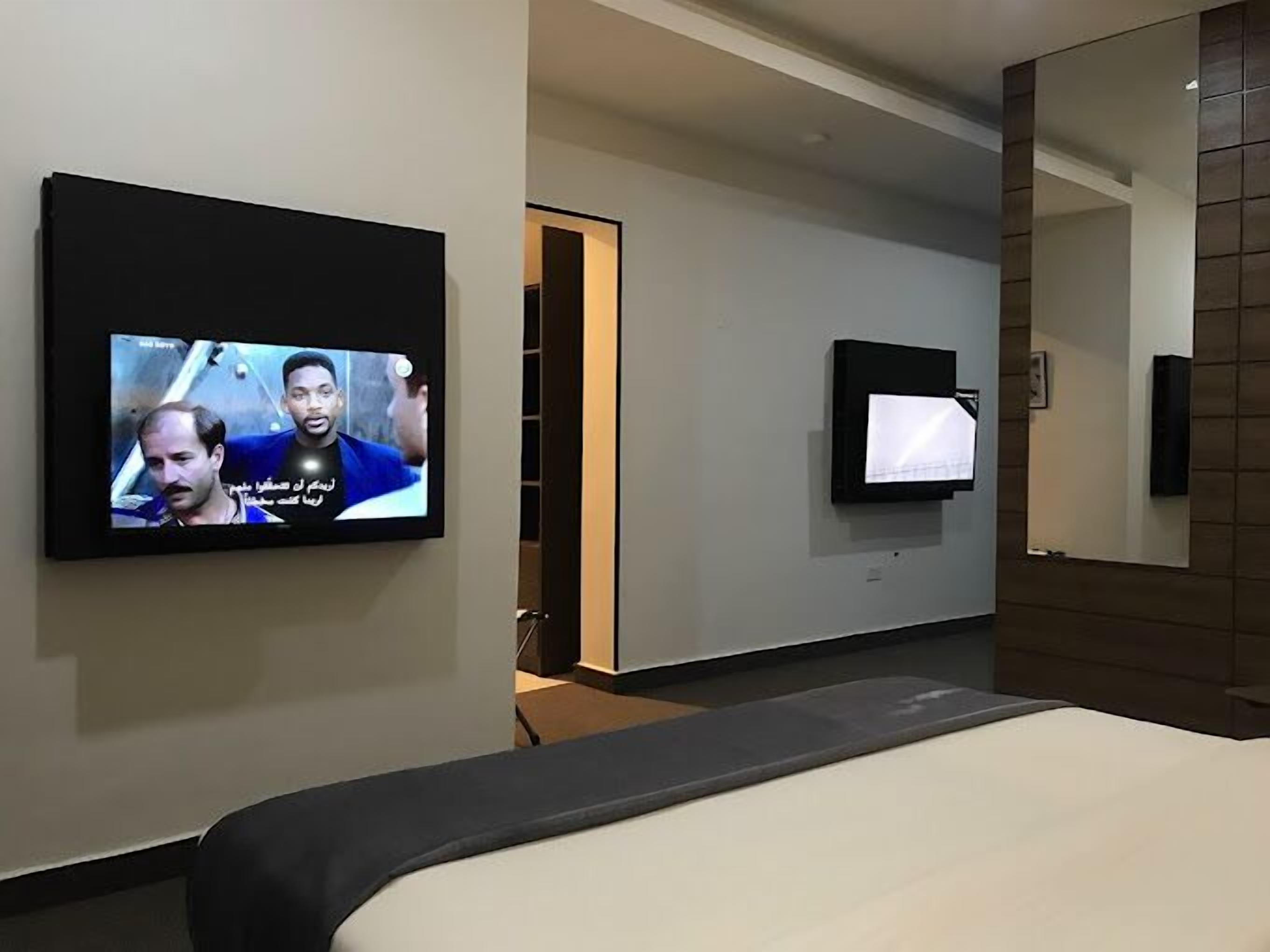 A hotel room with a bed, a TV mounted on the wall, and a mirror.