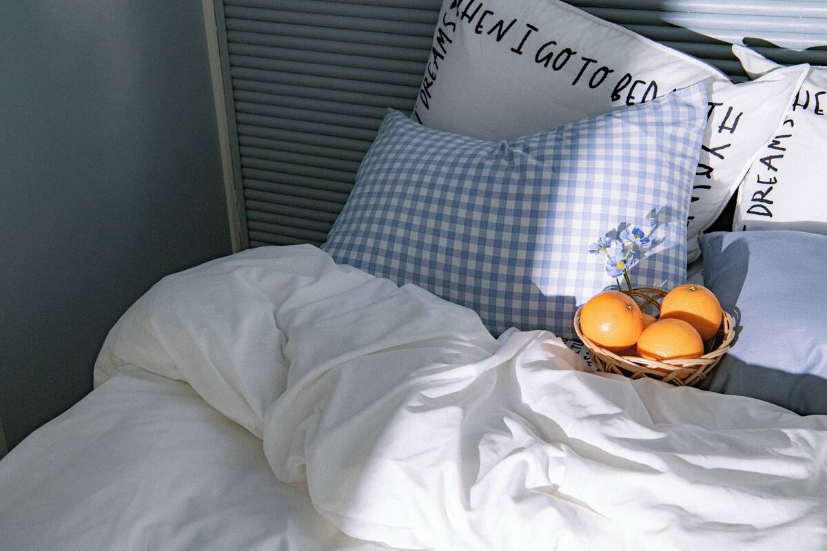 Cama bem arrumada com uma cesta de laranjas e um travesseiro xadrez.
