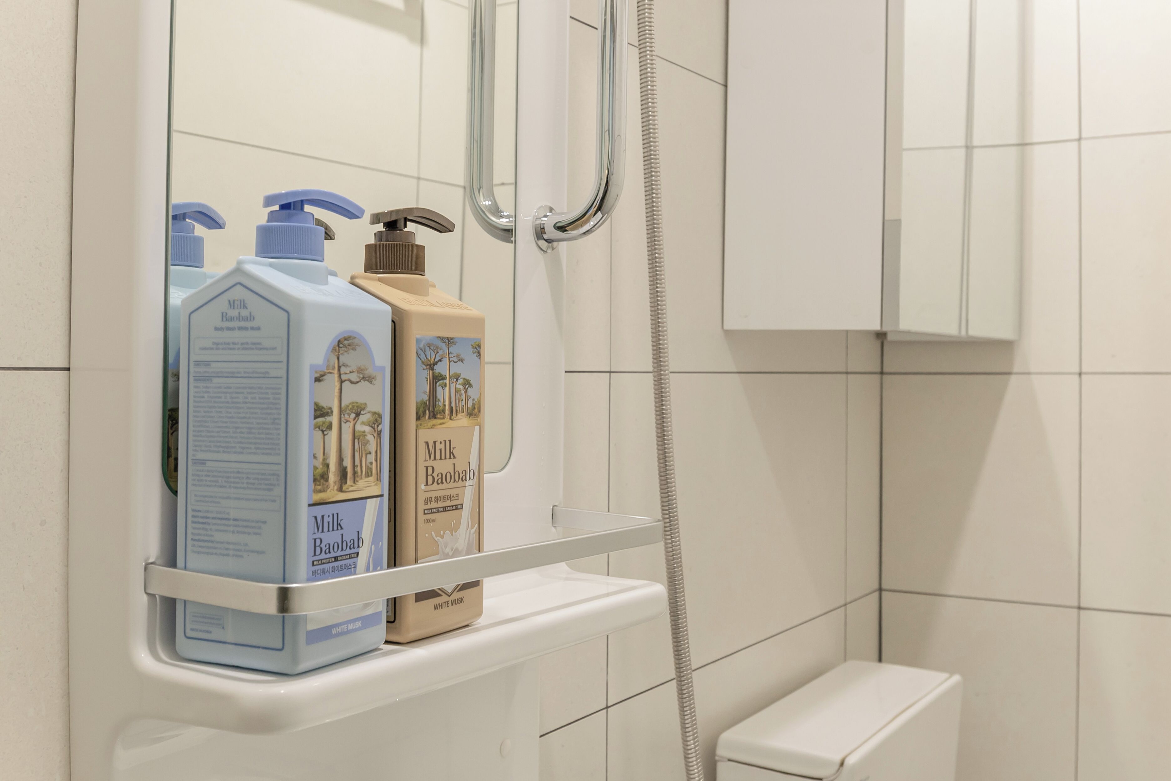 A bathroom with a white toilet, a shower, and a shelf holding two bottles of Milk Baobab soap.