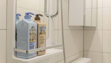 A bathroom with a white toilet, a shower, and a shelf holding two bottles of Milk Baobab soap.