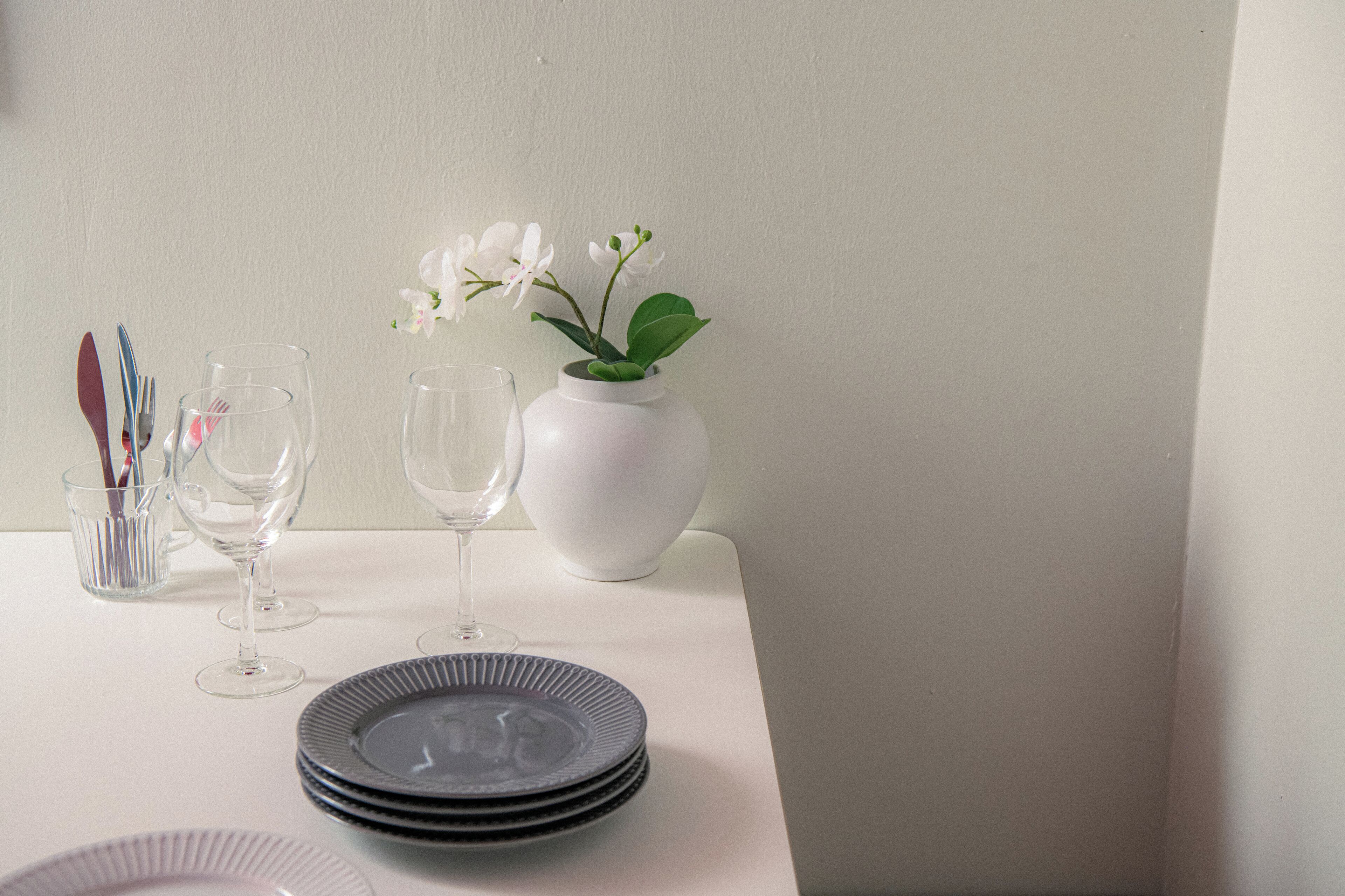 Et bord med en vase med hvide blomster, vinglas og stablede tallerkener.