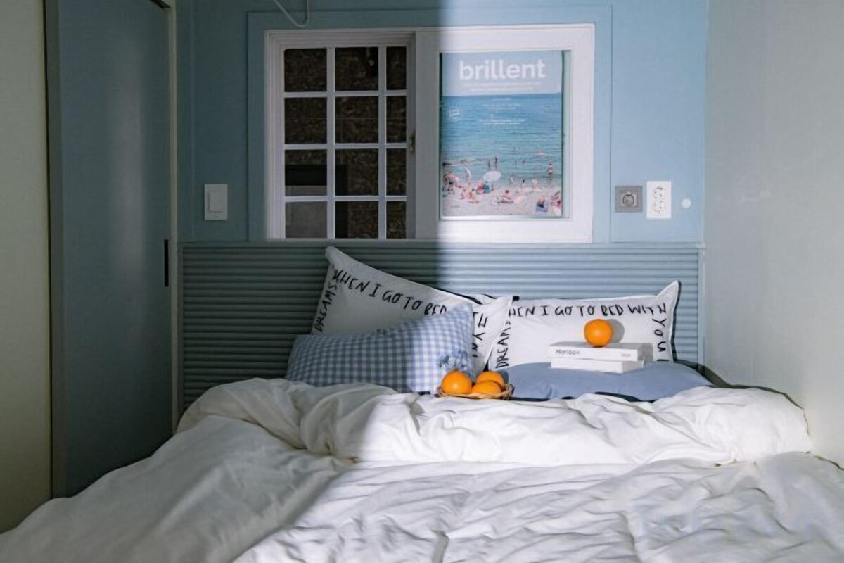 A bed with a checkered pillow, a pillow with text, and a pillow with a fruit design.