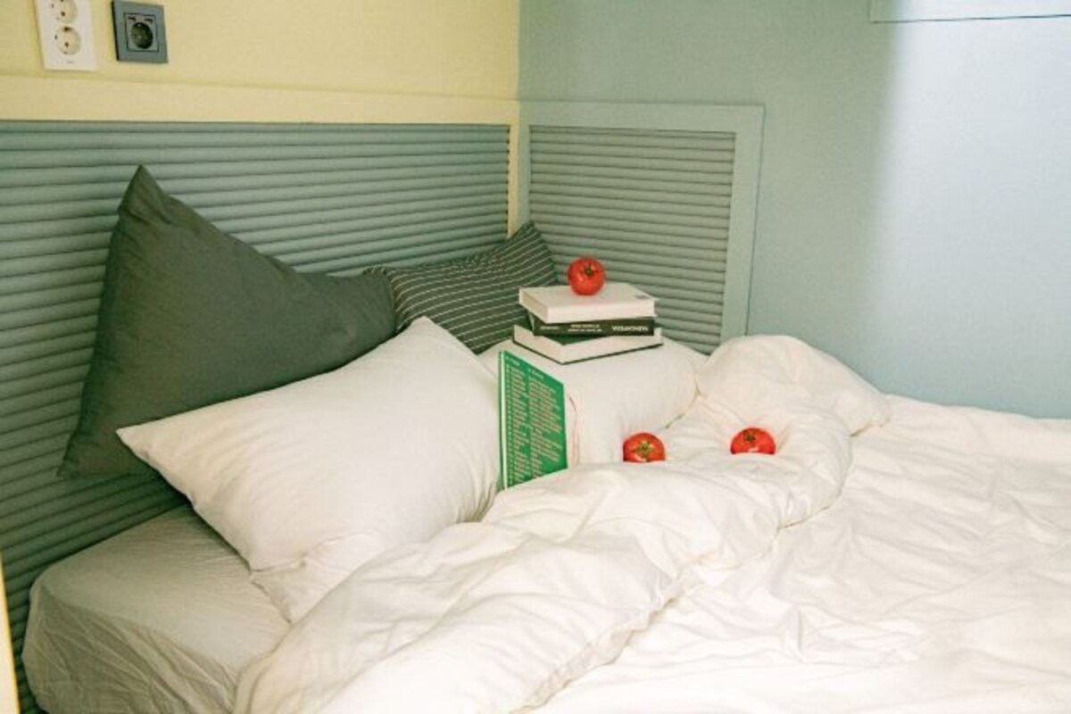 Una cama bien hecha con ropa de cama blanca, una almohada verde y dos libros apilados en la cabecera.
