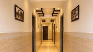 A hotel corridor with a marble floor, framed photographs on the walls, and a door at the end. - HOTEL THE ARCHI (Udaipur)
