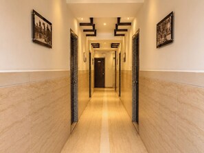 A hotel corridor with a marble floor, framed photographs on the walls, and a door at the end. - HOTEL THE ARCHI (Udaipur)
