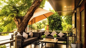 An outdoor seating area with a large tree, a sofa set, and a table with a bowl of fruit. - HOTEL THE ARCHI (Udaipur)