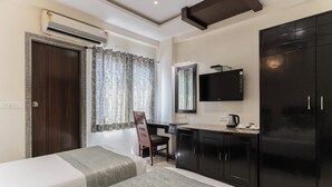 A hotel room with two beds, a desk, a TV, a wardrobe, and an air conditioning unit. - HOTEL THE ARCHI (Udaipur)