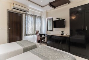 Een hotelkamer met twee bedden, een bureau, een televisie, een kledingkast en een airconditioning.