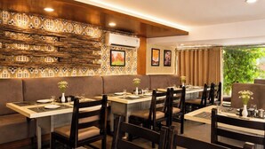 A restaurant with booths and tables, wooden paneling, and artwork on the walls. - HOTEL THE ARCHI (Udaipur)