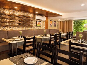 A restaurant with booths and tables, wooden paneling, and artwork on the walls. - HOTEL THE ARCHI (Udaipur)