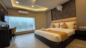 A modern hotel room with a large bed, a desk, and a view of the outdoors. - HOTEL THE GRAND AGASTYA (Singrauli)
