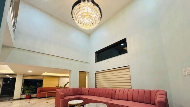 A spacious lobby with a large red sectional sofa, a round coffee table, and a chandelier. - HOTEL THE GRAND AGASTYA (Singrauli)