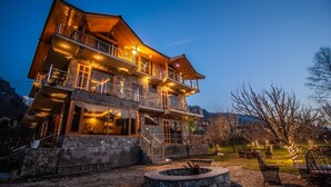 Un edificio de madera de varios pisos, con balcones, paredes de piedra y un hogar de piedra al frente.