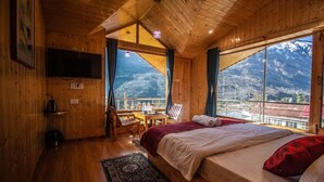 Una habitación de cabaña de madera con una cama, un televisor, una mesa y sillas, y vistas a las montañas.