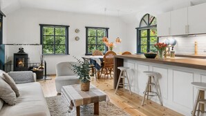 Eine moderne Küche mit einer zentralen Kochinsel, einem Essbereich mit Stühlen und einer gemütlichen Sitzecke mit Sofa und Hocker.