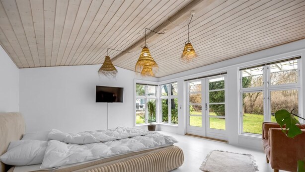 Ein modernes Schlafzimmer mit Bett, Fernseher und großen Fenstern.