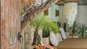 A tropical resort with a thatched-roof structure, a pool, and various plants.