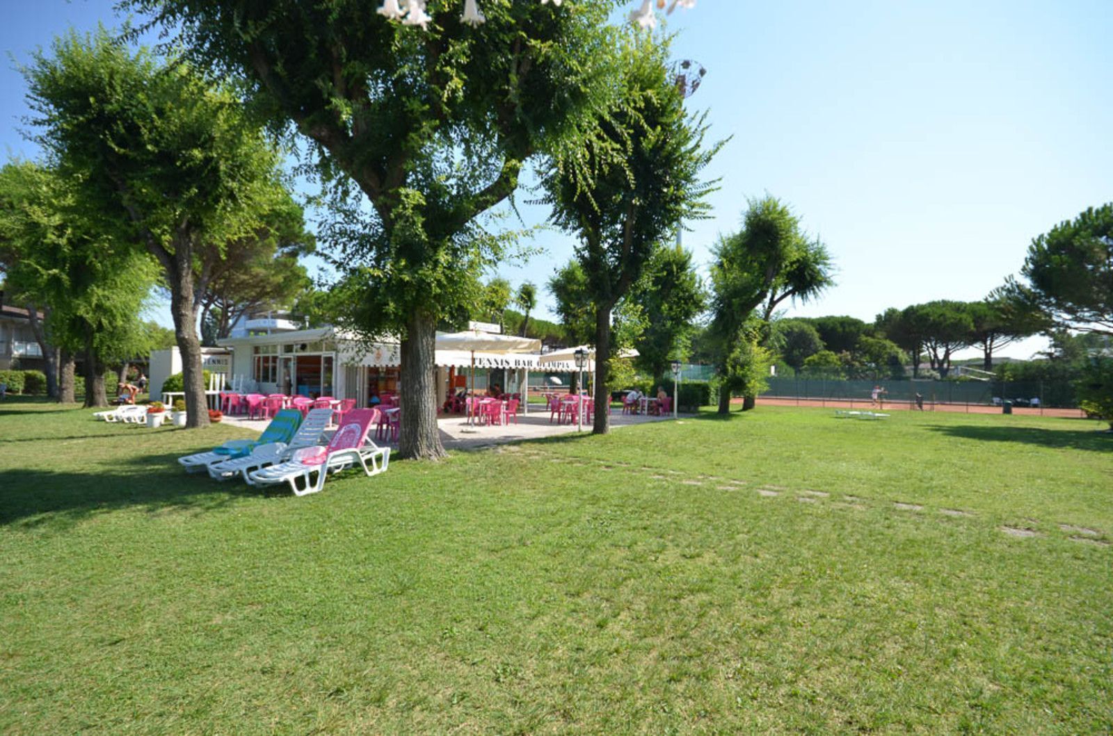 Un espacio al aire libre con césped, sillas de lounge y una zona de bar con mesas y sombrillas.