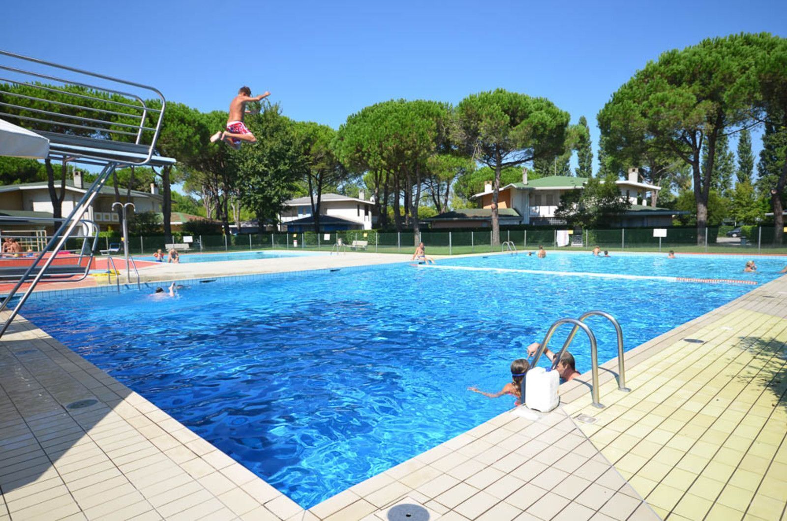 A swimming pool with a diving board and a tiled deck.