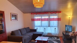 Una sala de estar con un sofá modular, una mesita, un televisor y una ventana con cortinas.