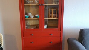 Un mueble rojo de madera con puertas de vidrio que alberga varios platos y cristalería.