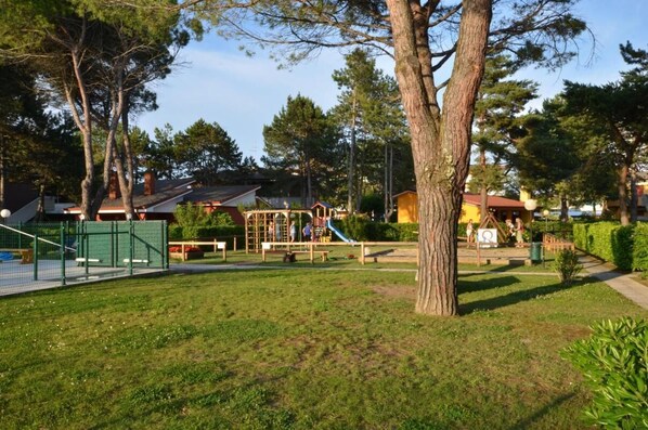 A playground with various play structures, surrounded by trees and a grassy area.