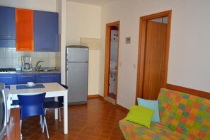 A compact kitchen with blue and orange cabinets, a refrigerator, and a dining area with a table and chairs.
