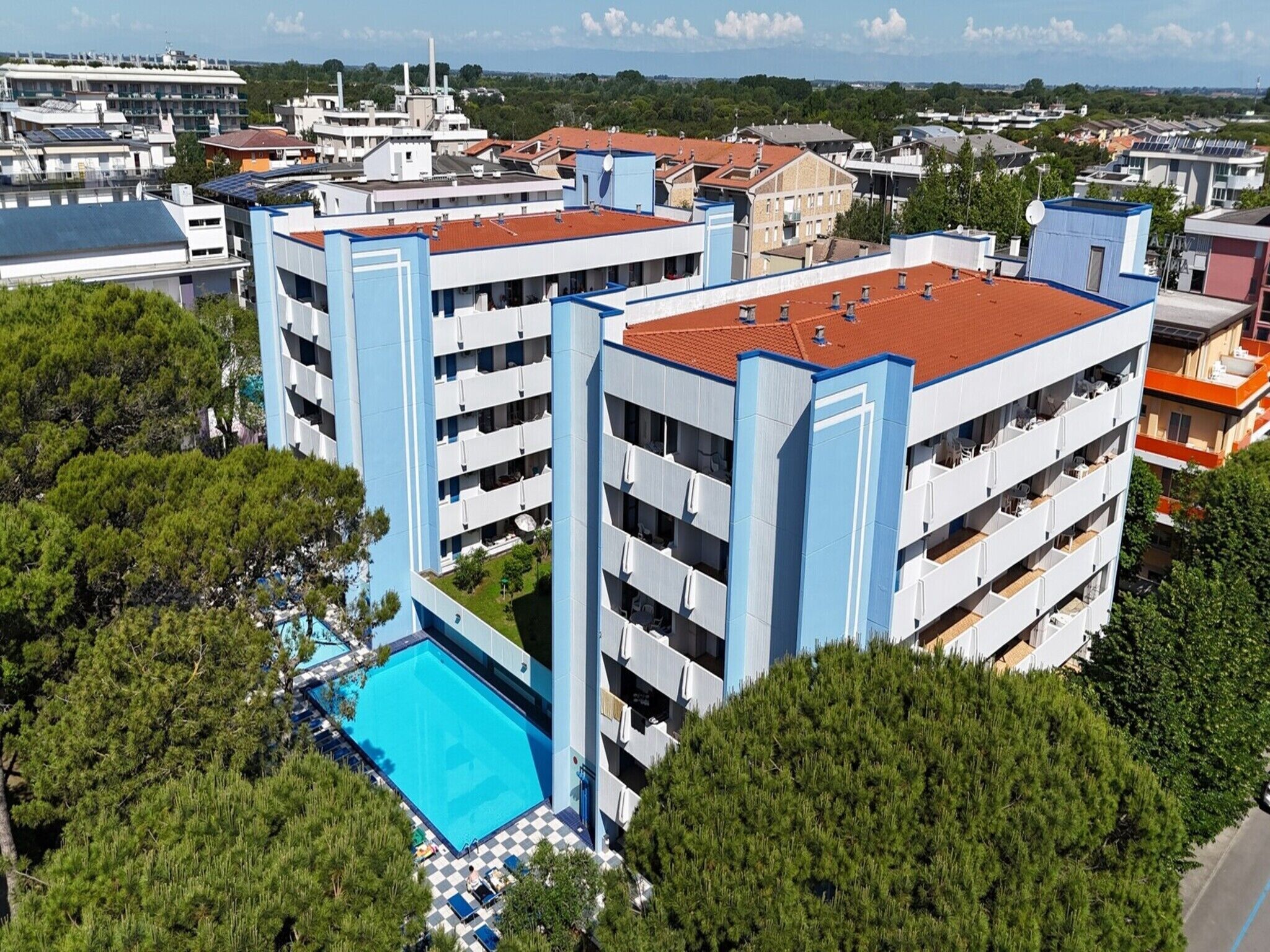 Un hotel de varios pisos con balcones, piscina y vistas de edificios circundantes.