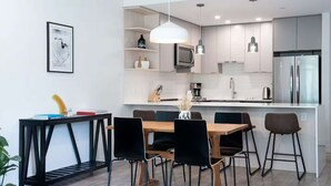 A modern kitchen with white cabinets, a central island, and a dining area with black chairs. - Breathtaking Condo with Panoramic Mountain Views (Revelstoke)
